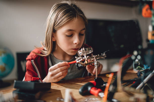 Girl learning robotics Girl wearing red hoodie looking circuit board throughout magnifying glass at home and building a robot science experiment kit for kids stock pictures, royalty-free photos & images