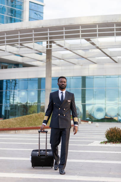 bluck airline pilot pulling his lagguge airport terminal - cabin crew pilot airport walking imagens e fotografias de stock