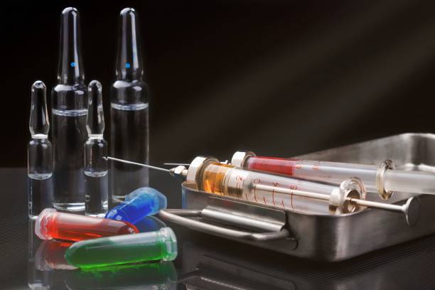 istock Syringes with medication on sterilization box, ampoules and vials with fluid on dark backround with light rays 898736516