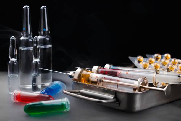 istock Syringes with medication on sterilization box, ampoules and vials with fluid on mist-covered surface 898736582