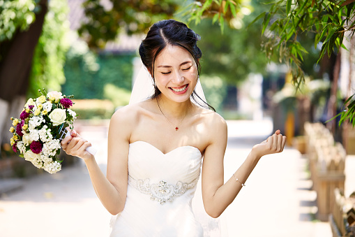 young and beautiful asian bride rejoicing with bouquet in hand on wedding day.