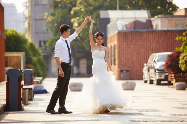 asian newlywed dancing outdoors young asian bride and groom in wedding dress dancing in parking lot. chinese wedding dress stock pictures, royalty-free photos & images