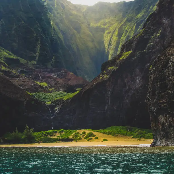 Stunning view of secluded Kalalau Beach and Kalalau Valley from a boat on a sunny day, Na Pali Coast, Kauai, Hawaii