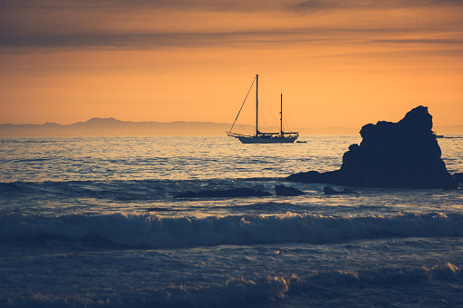 Silhouette of a sailboat at sunset sailing from Newport Beach, California with Santa Catalina Island in the background