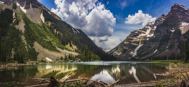 Panorama of Pyramid Peak (left), Maroon Bells (right), and Crater Lake in Snowmass Wilderness in Aspen, Colorado with a blue sky and clouds in summer