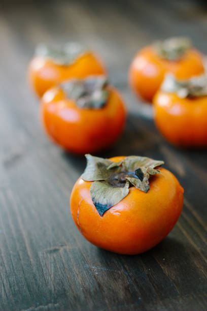 istock Fresh orange persimmons upside on wooden table. 898784730
