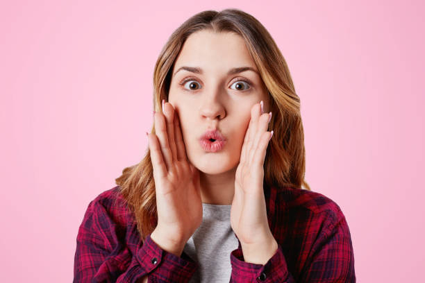 istock Amazed pretty lovely woman rounds lips as says wow, keeps hands on cheeks, being shocked, gestures in studio, isolated over pink background. Attractive young female model gossips with friends 898794200