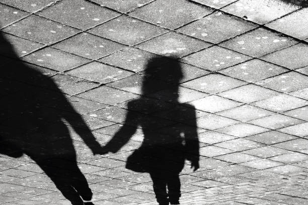 Mother and daughter holding hands  shadow , on city street sidewalk in black and white