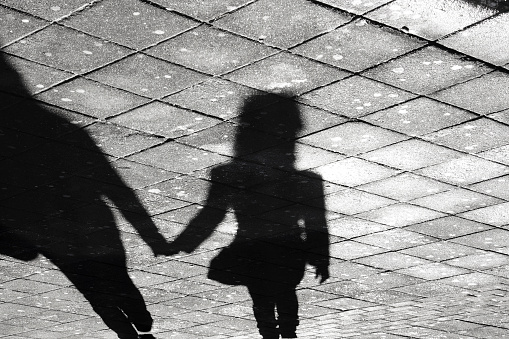 Mother and daughter holding hands  shadow , on city street sidewalk in black and white