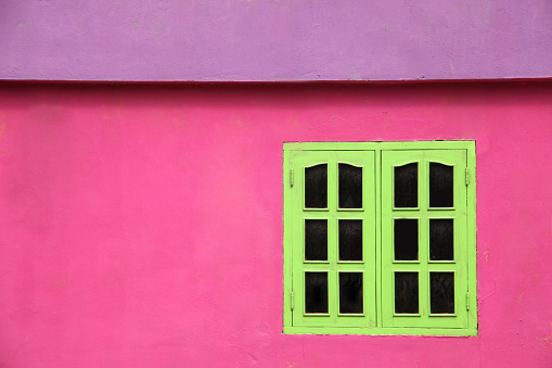 Close up of a brightly coloured building with pink walls, lime green windows & purple roof, Caribbean.