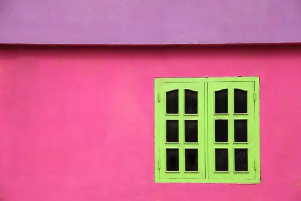 Photo of Close up of a brightly colored building with pink walls, lime green windows & purple roof, Caribbean.