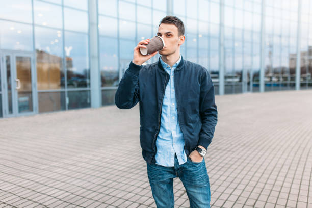 istock a man walks around the city and drinking coffee from a paper Cup, a handsome guy walks around and resting, the guy on the background of a modern building, office 898818076