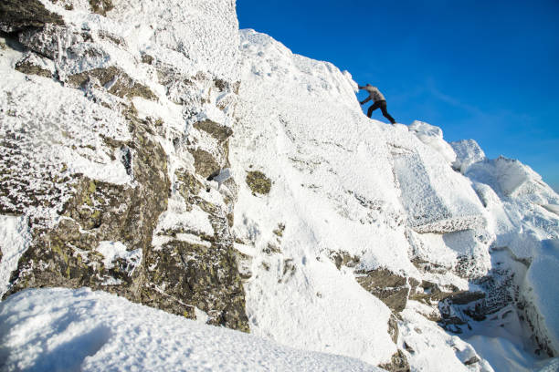 der bergsteiger den gipfel klettern bedeckt mit eis und schnee, mann wanderer gehen auf dem gipfel des felsens. winter-saison. - conquering adversity blue rock climbing ice climbing stock-fotos und bilder