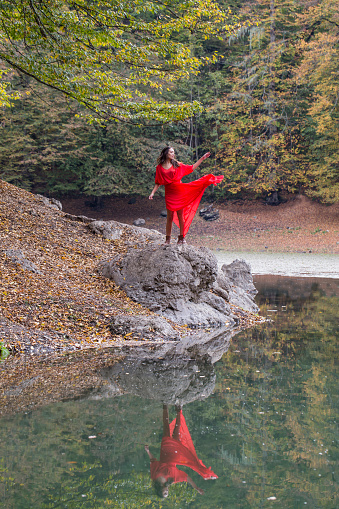 girl in the autumn forest. fairy-tale reflection in the lake. Fashionable woman standing over lake in park