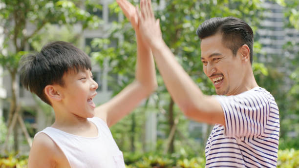 Asian father & son giving a high five after scoring outdoors in morning stock photo