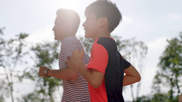 low angle view fo Chinese man & son jogging outdoors in garden back lighted