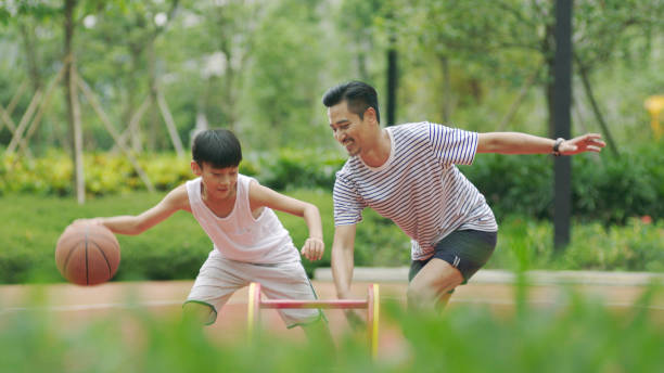 padre asiatico e figlio che giocano a basket in giardino al mattino - park child asia lifestyles foto e immagini stock