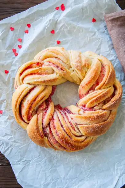 Raspberry jam swirl brioche wreath on baking paper on a wooden background.