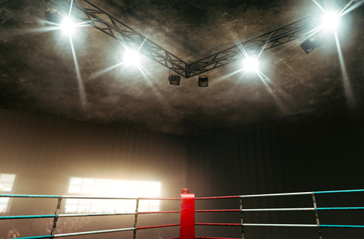 A regular boxing ring surrounded by ropes spotlit in the missle on an isolated dark background