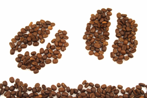 Roasted coffee beans lie all over the frame on a surface with a mottled gray texture. There is space for text in the center of the frame. View from above
