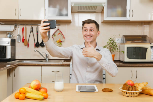 istock Handsome young business man in plaid shirt having breakfast, sitting at table, doing selfie on mobile phone, eating cereals with milk on light kitchen. Healthy lifestyle. Cooking at home. Prepare food 898886306