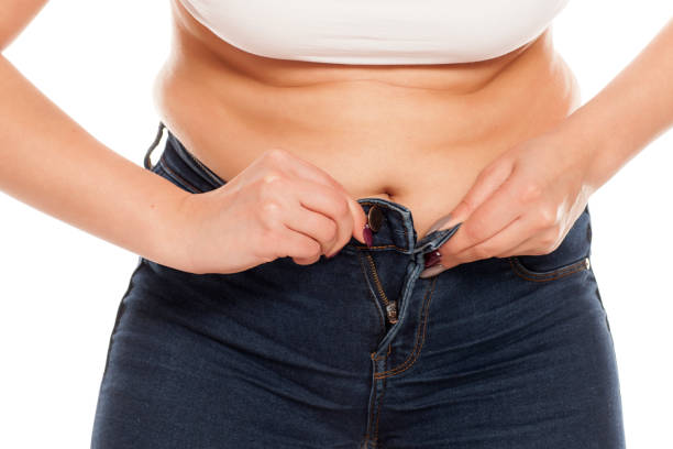 a young woman has difficulty buttoning her jeans - too small imagens e fotografias de stock