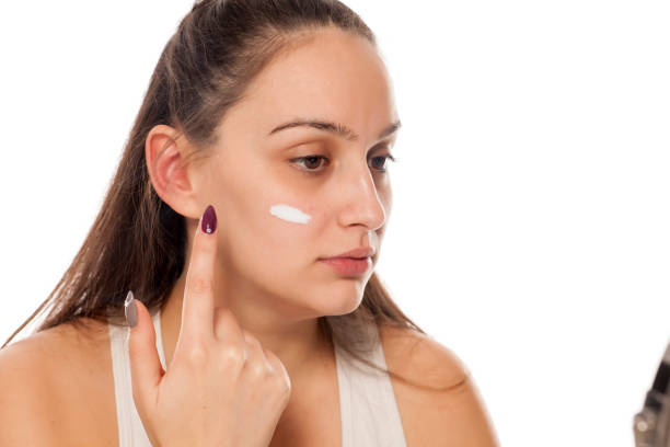 istock a young, pretty woman applying cream on her face 898900910