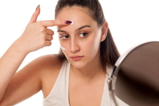istock a young, pretty woman applying cream on her face 898901090
