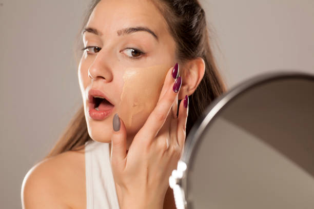 young woman applying a liquid foundation on her face with her fingers