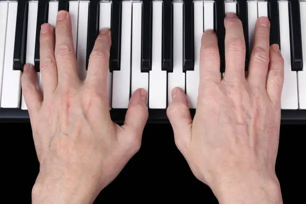 An elderly retired man plays an old melody on the keyboard of the synthesizer. Studio human eyes view  shot. Partially isolated on black with patch