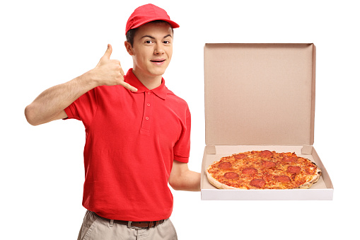 Teenage pizza delivery boy holding a pizza box and making a call me gesture isolated on white background