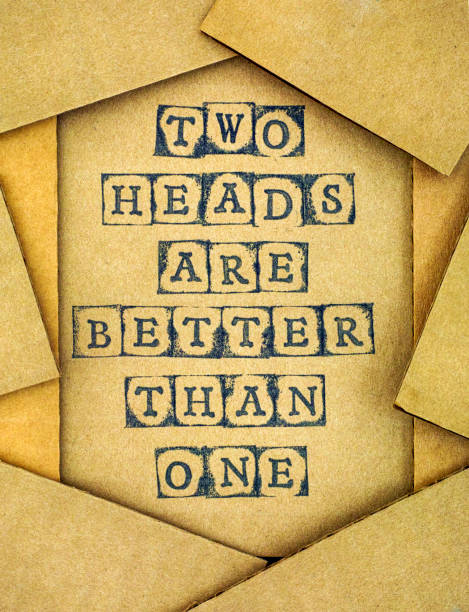 Phrase Two Heads Are Better Than One make by black alphabet stamps on cardboard with some piece of cardboard.