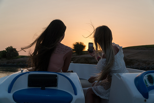Girls ride a boat on the channels of the city of El Gouna and make photo on a mobile phone.