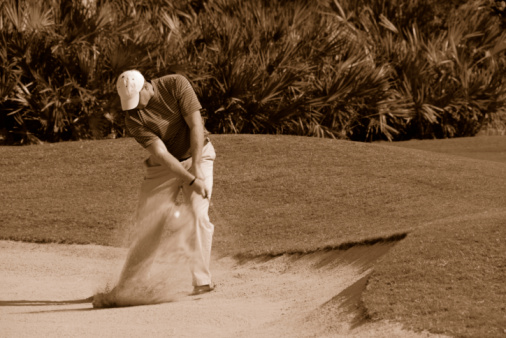 Asian player swinging club in sand trap of a course