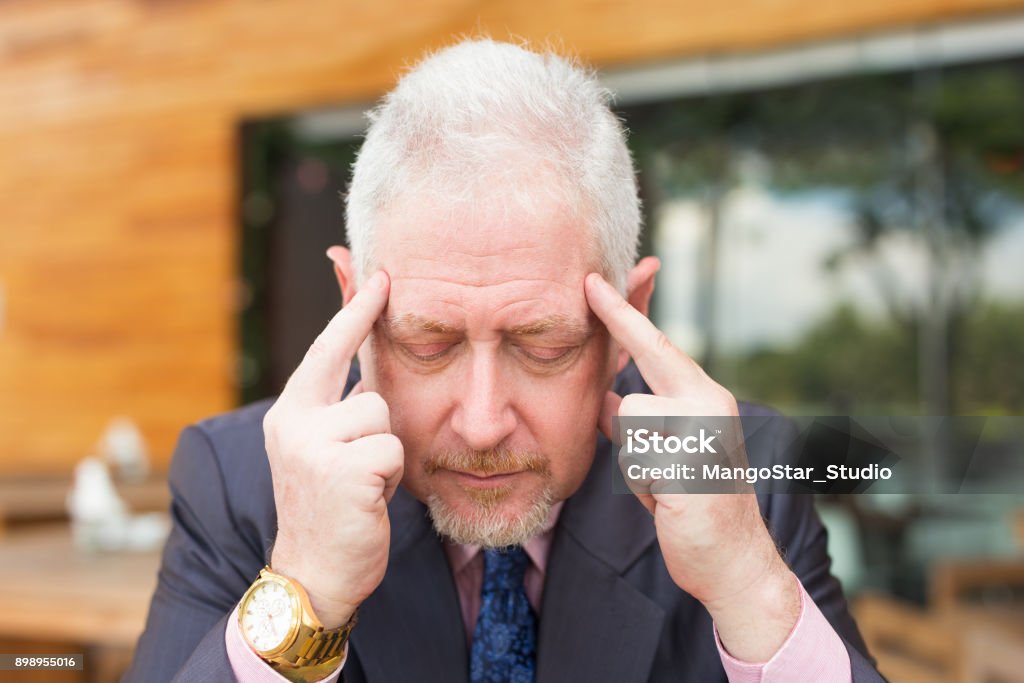 Closeup of Thoughtful Business Man Outdoors Closeup portrait of thoughtful senior handsome man touching head with fingers and with his eyes closed in outdoor cafe. Front view. Adult Stock Photo