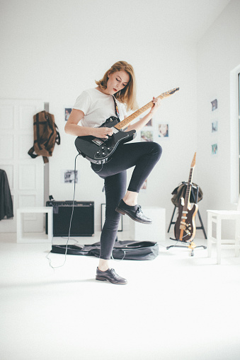 Young woman playing electric guitar. Guitar head is changed, and it's not a copy of any existing guitar. Guitar head does not look like any other existing guitar head.