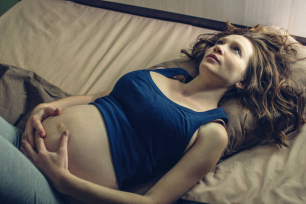 Pregnant woman feeling pain in her belly lying in bed with insomnia at night. Concept of pregnancy and health stock photo