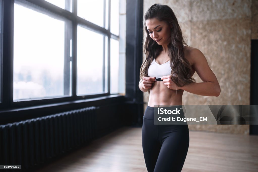 Female fitness model in white top and black leggings is posing near the big windows in studio in morning time Abdominal Muscle Stock Photo