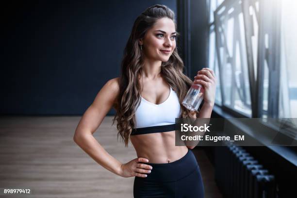 Modelo De Fitness Femenino En Blanco Superior Y Negros Polainas Está Posando Cerca De Las Ventanas Grandes En El Estudio En El Tiempo De Mañana Foto de stock y más banco de imágenes de Ejercicio físico