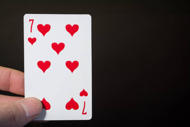 istock Abstract: man hand holding playing card seven of hearts on a black background with copyspace 898983490