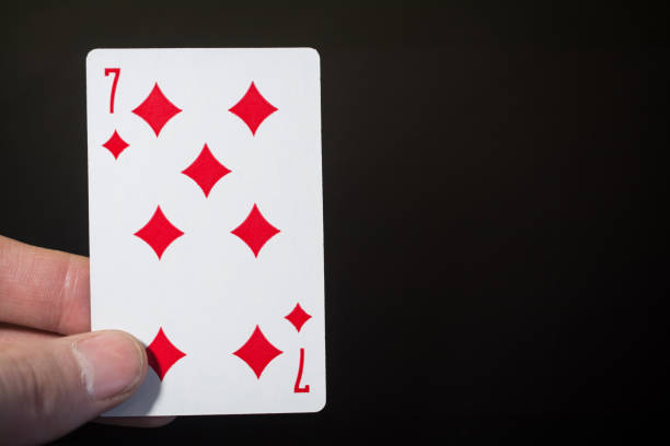 istock Abstract: man hand holding playing card seven of Diamonds on a black background with copyspace 898983716