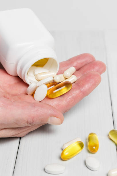 istock Woman hands hold vitamin complex and dietary supplement, pours from white bottle into palm yellow capsules of omega 3, white pills of calcium and glucosamine on wooden planks table 898984792