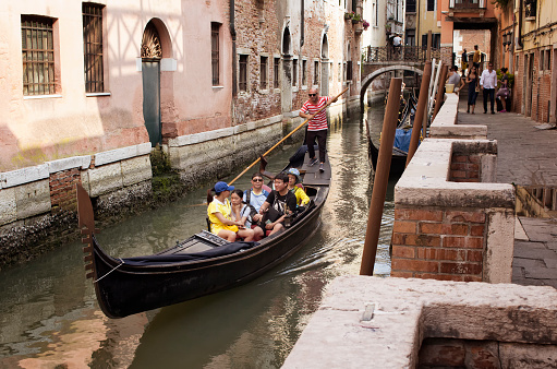 Asian family ride gondola tour in Venice / Italy. Old, historical buildings in the background.