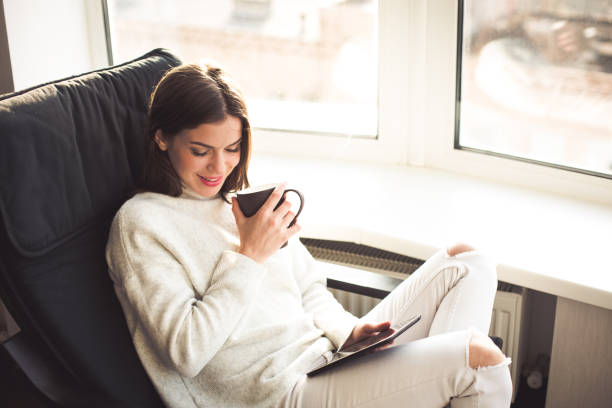 istock Woman sitting by the window with an e-book 898989600