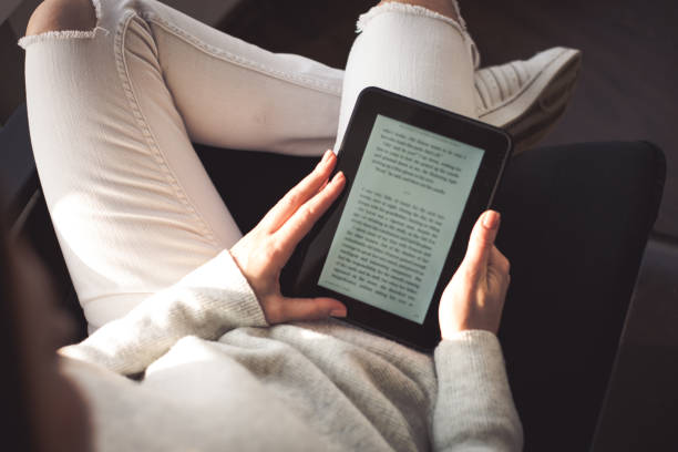 istock Woman sitting by the window with an e-book 898991896