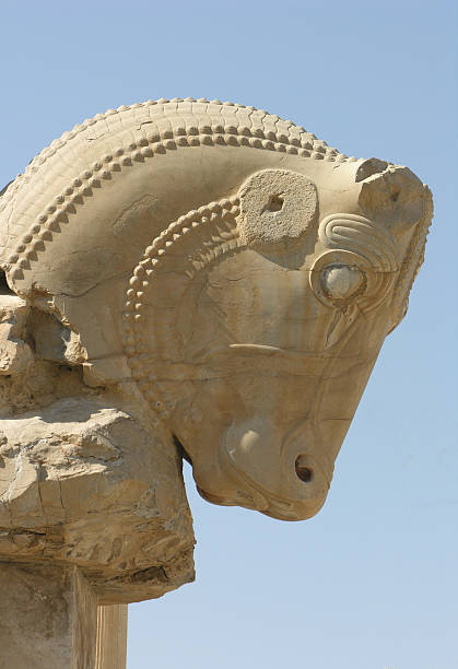 Twin Homa or Huma the Griffin bird figures used as decorative capital statuary of a column in Persepolis of Shiraz against blue sky with white fluffy clouds.