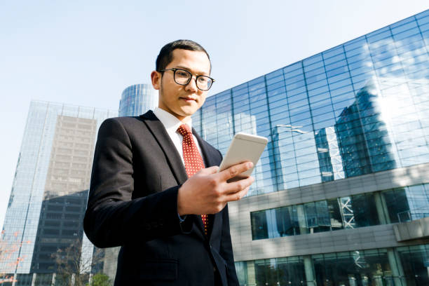 istock young businessman holding smartphone outside office building 899043006