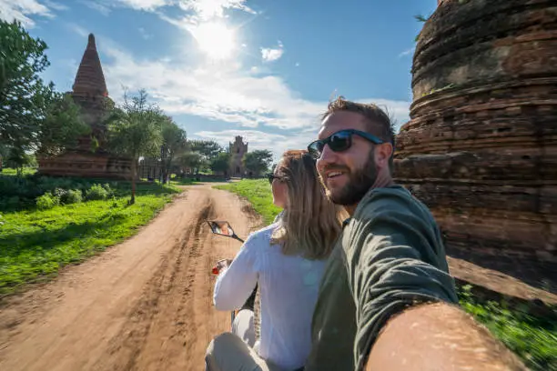 Shot of a carefree young couple taking a selfie while riding on a scooter, temples pagodas and monastery coming out from the lush greenery. People travel concept.