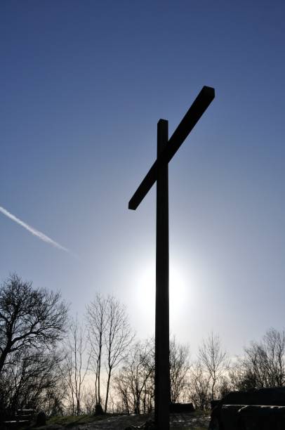 Iron Cross with Sunbeam, Trees and Contrail Hilltop iron cross with sunbeam, trees and contrail in the background and boulders in the forefront. hope god lighting technique tree stock pictures, royalty-free photos & images