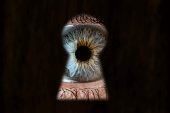 Female blue eye looking through the keyhole. Concept of voyeurism, curiosity, Stalker, surveillance and security